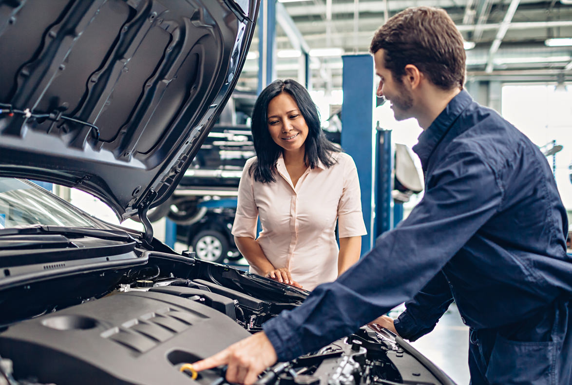 Mecánico de Vala Automotriz atendiendo a clienta — revisión de motor con cofre abierto en taller de Texcoco